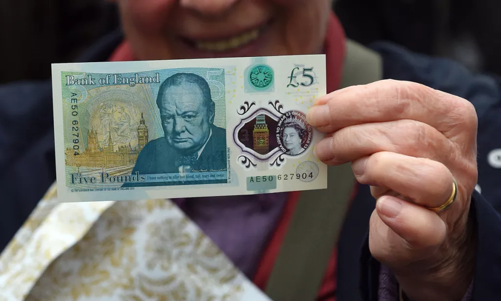 A woman holds up a new £5 (6.5 euros, $7.2) banknote bearing the image of wartime leader Winston Churchill at its unveiling by the Bank of England at Blenheim Palace in Woodstock on June 2, 2016.  The note, to be rolled out from September, is the first to be printed on polymer -- a thin, flexible plastic film that is seen as more durable and secure and is already used in Australia and Canada. / AFP PHOTO / POOL / Joe Giddens