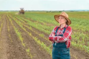 Worried female farmer standing in corn field and looking over cr