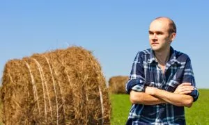 morning portrait of farmer in field against wheat bales